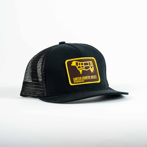 Black trucker cap with yellow and brown patch that includes cow outline and carter country meats wyoming usa