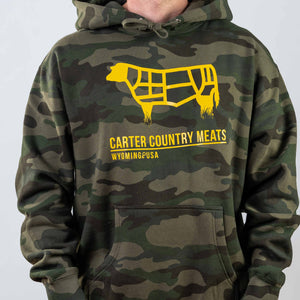 Modeled front view camo hoodie with yellow cow outline and yellow carter country meats wyoming usa text
