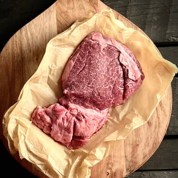 Raw cheek meat on open paper wrapping atop round cutting board