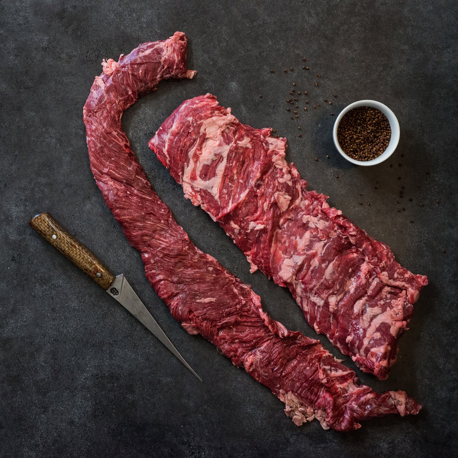 2 large skirt whole skirt steaks on a slab with a cup of spices and a knife
