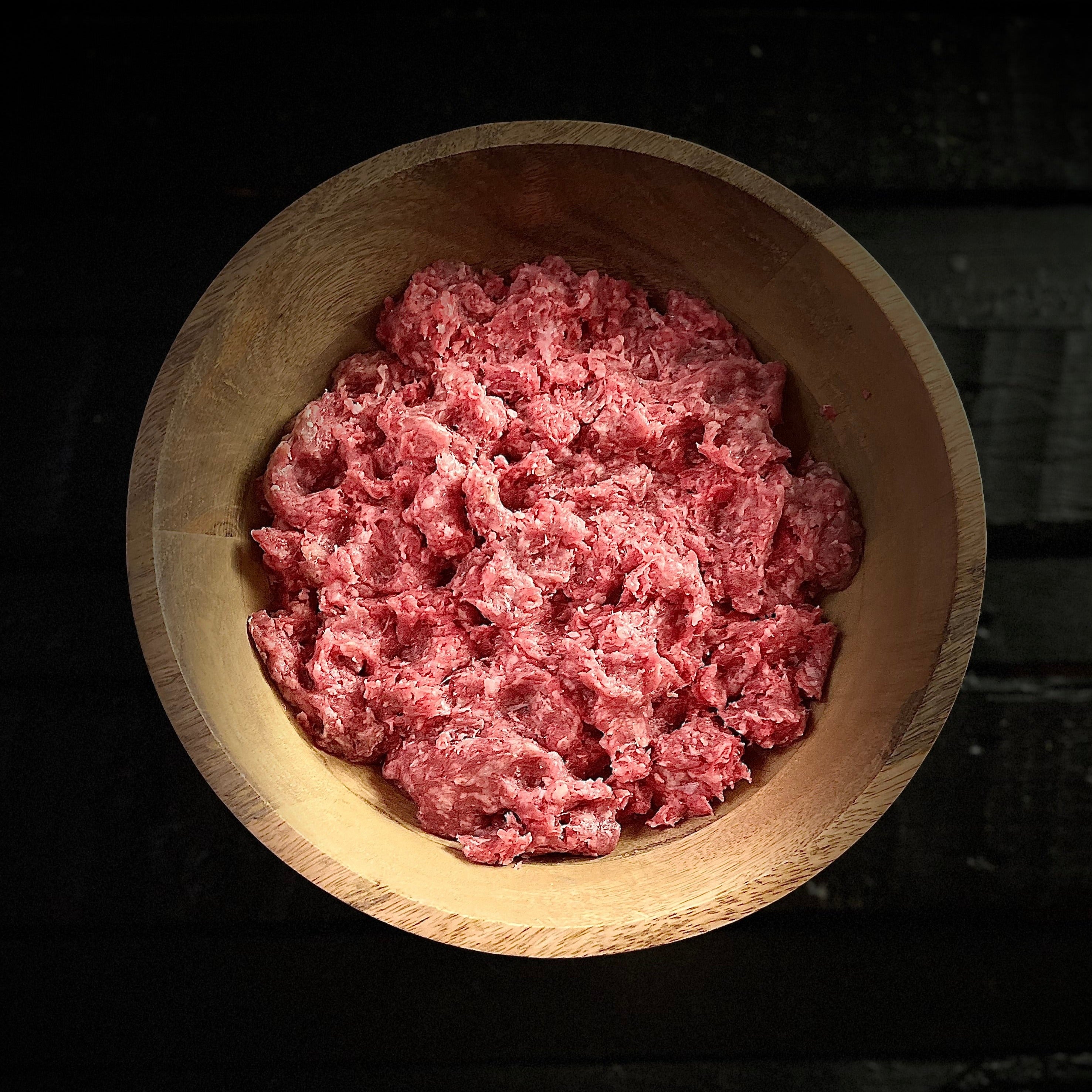 Raw ground beef spread out in wood bowl on slab