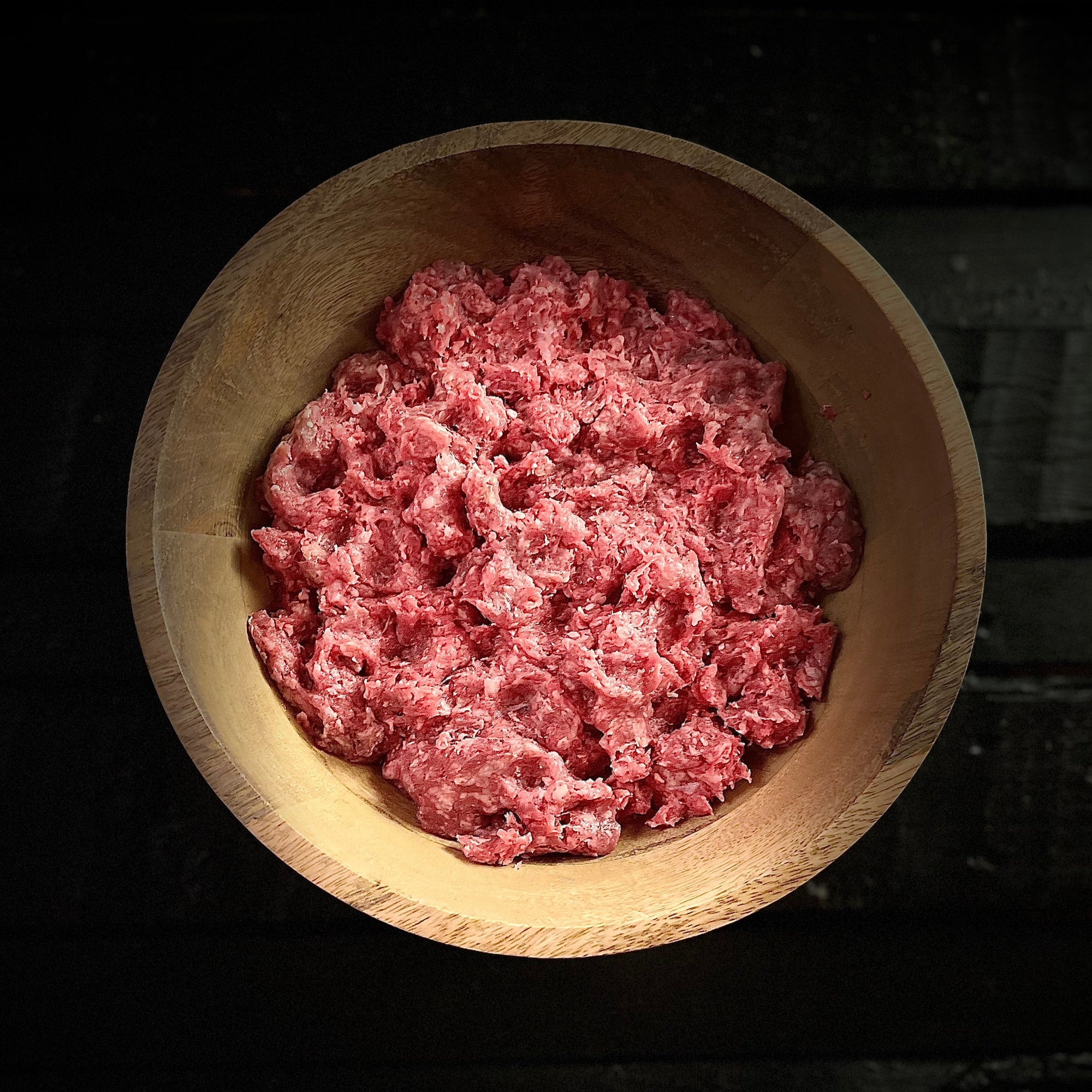 Raw ground beef spread out in wood bowl on slab
